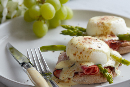 breakfast, eggs, plate, benedict, dish, food, ham, brunch, poached, muffin, hollandaise, meal, toast, bread, asparagus, vegetable, gourmet, grapes, fruit, knife, fork