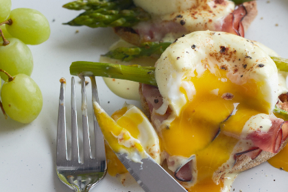 breakfast, eggs, plate, benedict, dish, food, ham, brunch, poached, muffin, hollandaise, meal, toast, bread, asparagus, vegetable, gourmet, grapes, fruit, knife, fork, eating, yolk
